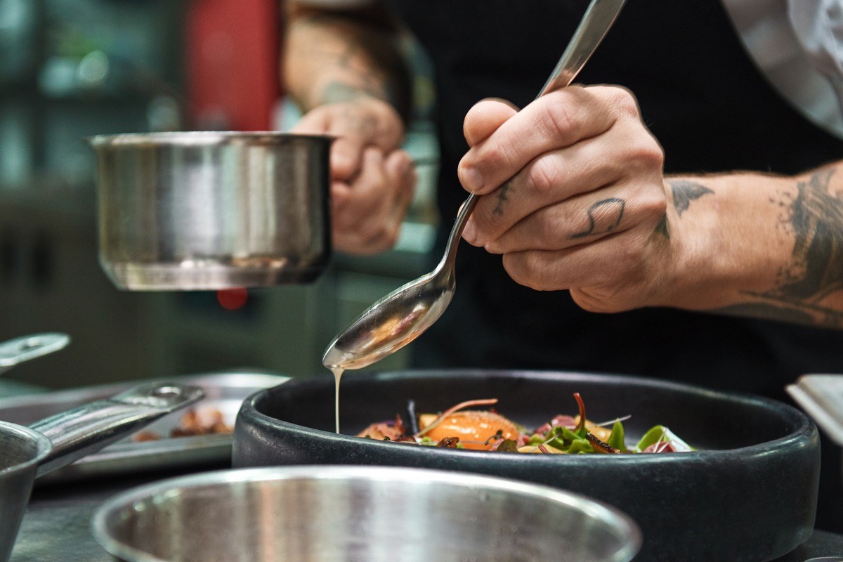 Secret recipe. Close up photo of chef hands with several tattoos adding a sauce to italian pasta Carbonara. Food concept